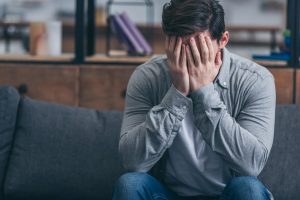 man sitting with head in hands on couch